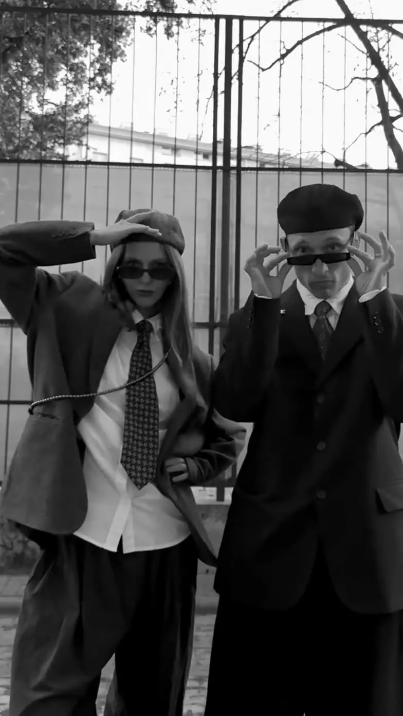 Black and white: Sergei and Elvira in suits and sunglasses posing by an iron fence
